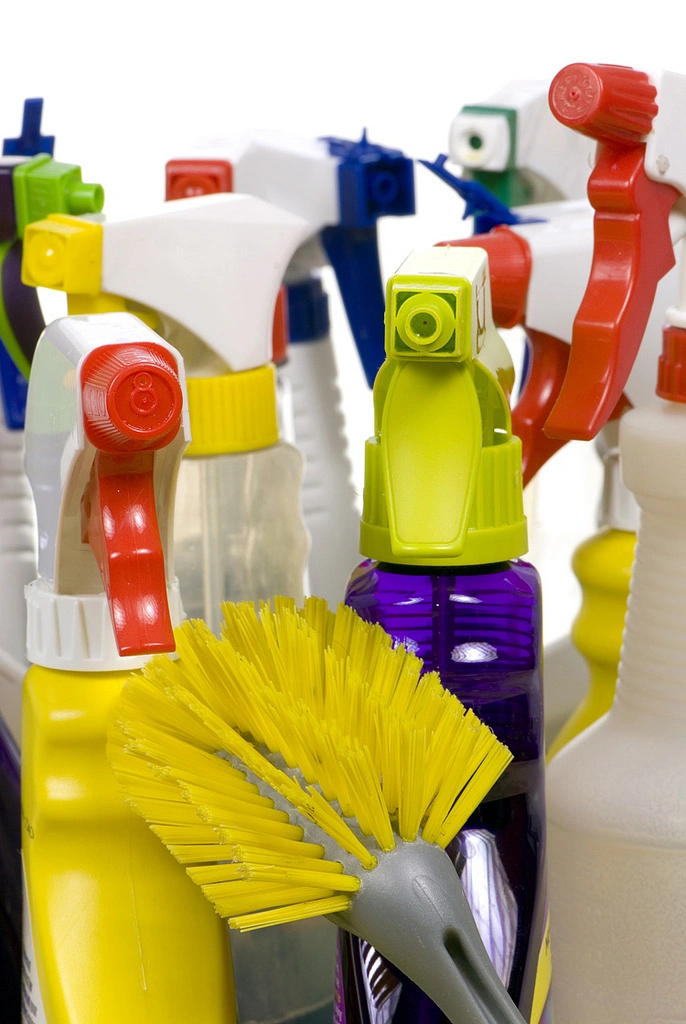 A yellow scrub brush in front of a collection of bathroom cleaner bottles. Photo Cred: Backdoor Survival on Flickr.
