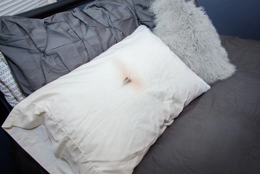A white pillow on a bed with makeup stains on the pillowcase