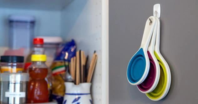 The interior of a kitchen cabinet with measuring spoons hung from a hook