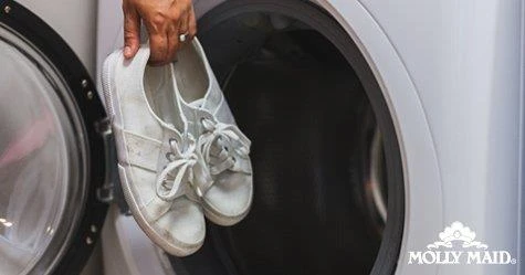 Person putting dirty white shoes in a washing machine