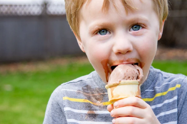 little boy in striped shirt eating chocolate ice cream out of a cone.