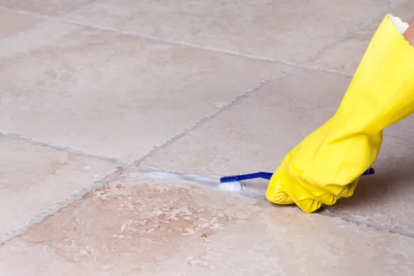 Gloved hand cleaning tile grout with toothbrush