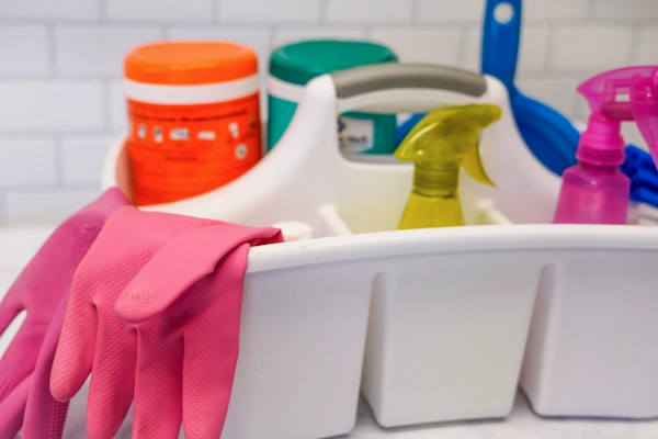 Pink rubber gloves and assorted colorful cleaning products in white plastic cleaning caddy.