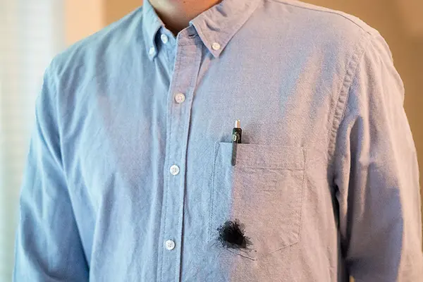 Close-up of man in blue button down shirt with pen in breast pocket leaking spot of black ink.