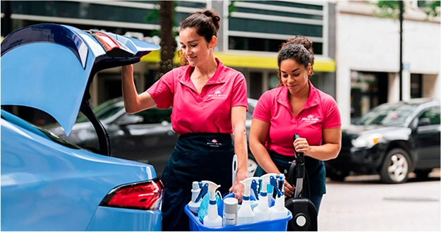 Two Molly Maid cleaning experts unloading supplies from the trunk of a car.