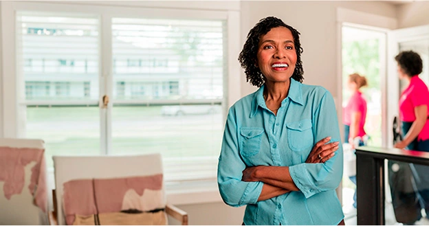 Molly Maid customer standing in her living room with maids entering the house behind her.