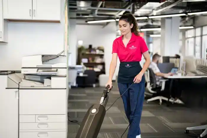 Cheerfully Molly Maid professional vacuuming a corporate office.