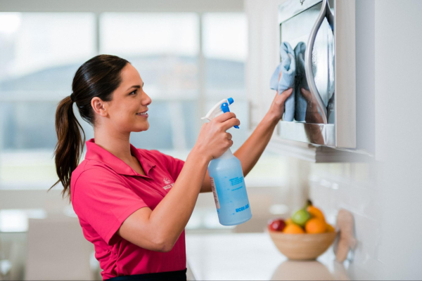 A Molly Maid service professional cleaning a microwave.