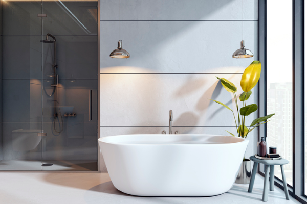 A pristine standalone bathtub in a clean, well-lit bathroom with overhanging lights and a plant