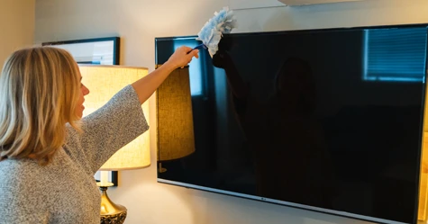 woman dusting television on the wall
