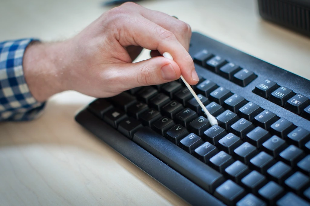 Person's hand cleaning in between computer keyboard keys with a Q-tip