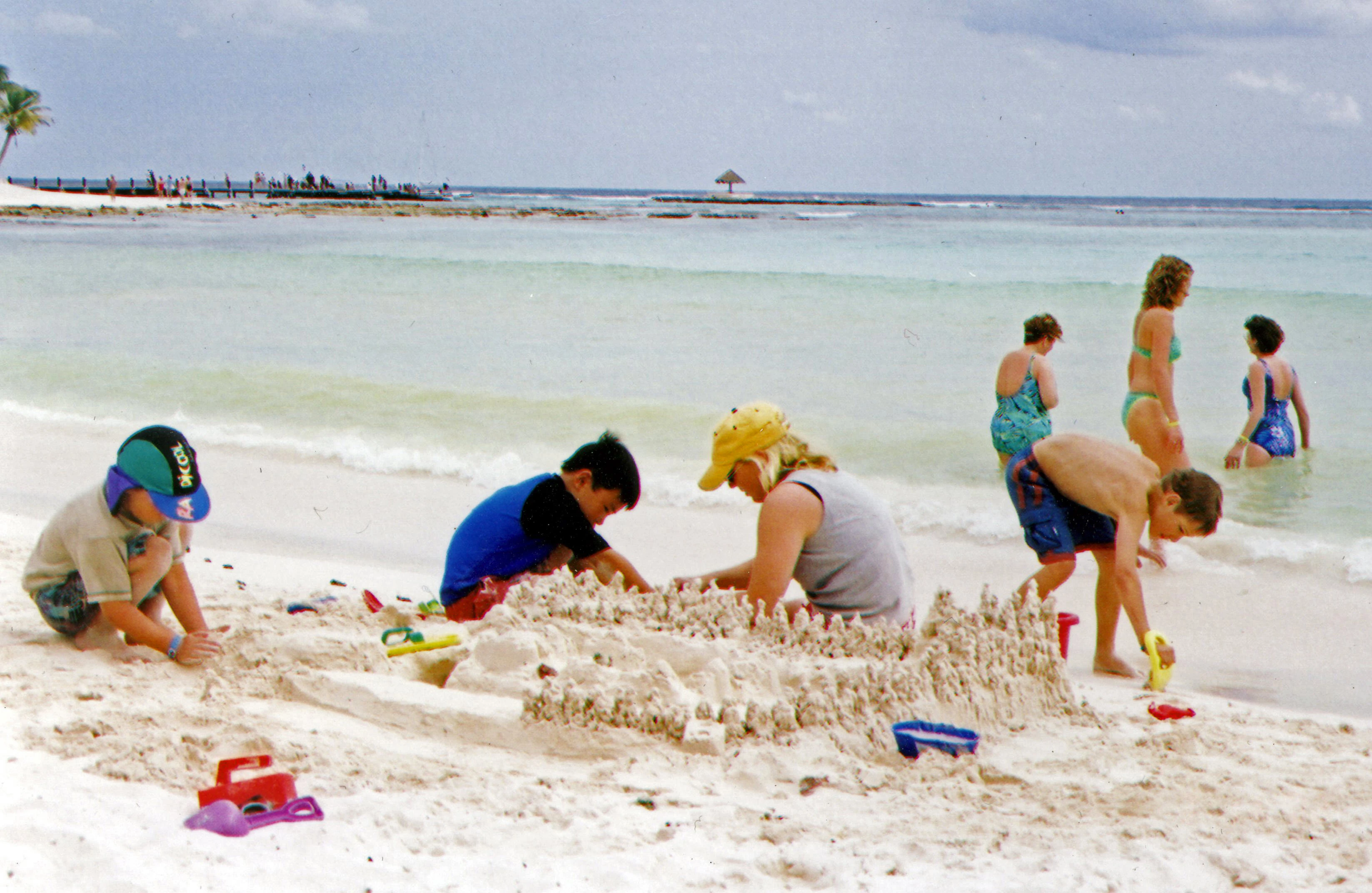 Kids building a sandcastle on the beach with the ocean and a few people in the water in the background