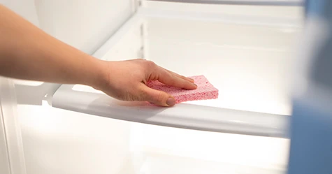 A person wiping the inside of a refrigerator with a sponge