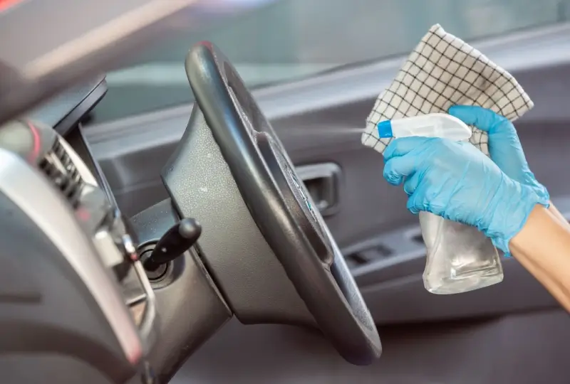 Person disinfecting steering wheel in a car.