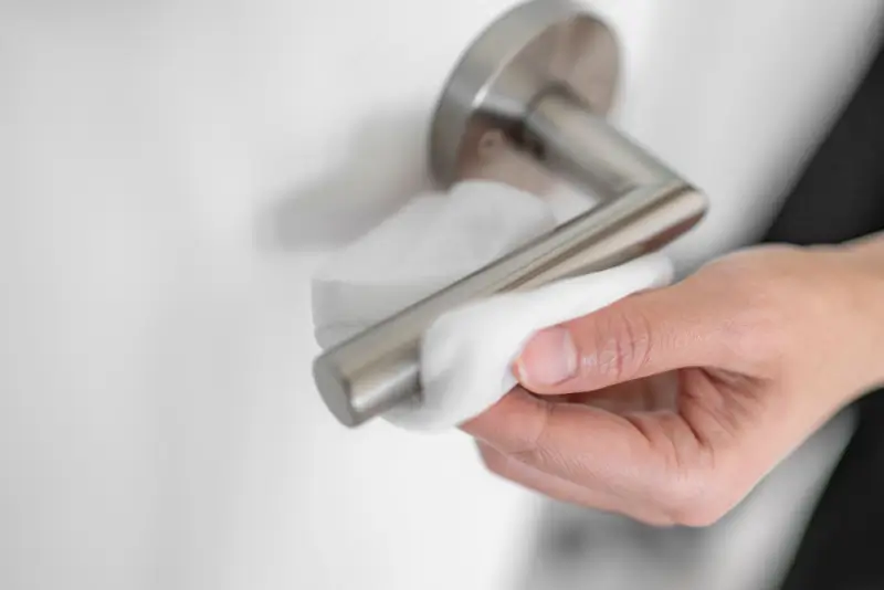 Person using sanitizing wipe on a doorknob.