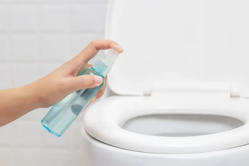 Person using disinfecting spray on toilet.
