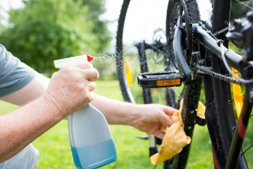 man using a spray bottle and yellow cloth to clean a bicycle