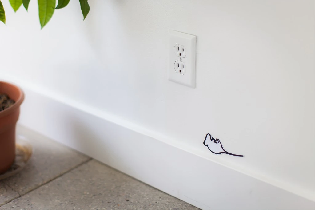 A wall in a home with a whimsical sticker of a mouse lying on its back