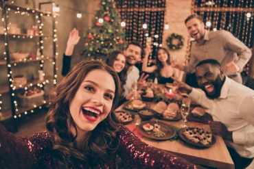A young woman taking a photo of friends gathered around dining room table celebrating with a holiday meal.