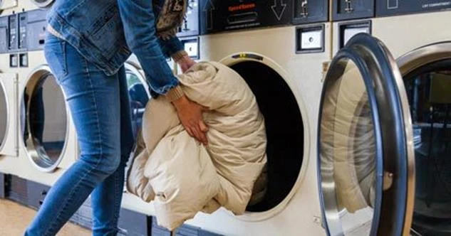 Woman putting a comforter into a washing machine at a laundromat
