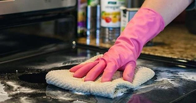 Person wearing a pink rubber glove cleaning a black stovetop with a cloth
