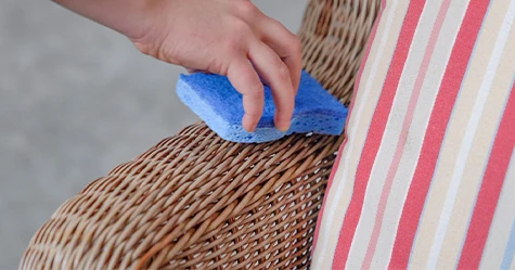 Person wiping a wicker chair with a sponge