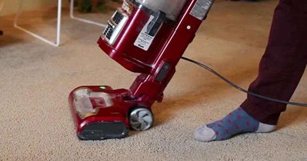 Person vacuuming carpet with a red vacuum