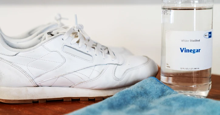 White sneakers next to a bottle of white vinegar and a cloth