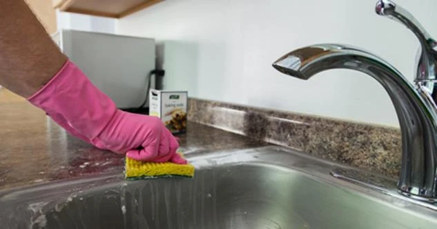 Person wearing a pink rubber glove cleaning a sink with a sponge