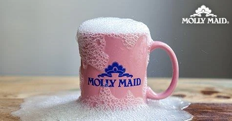 A sudsy pink coffee mug with the Molly Maid logo on a wood table
