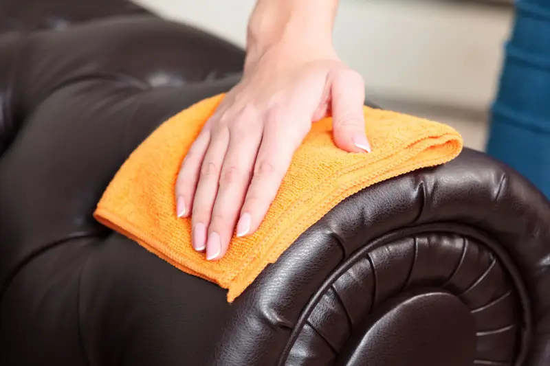 Hand wiping brown leather sofa with a cloth.