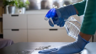 Person wearing blue rubber gloves using a bleach solution in a small plastic spray bottle to clean countertops.