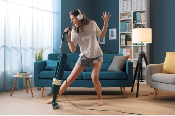 Cheerful woman cleaning up her home and singing, using the vacuum cleaner as a microphone