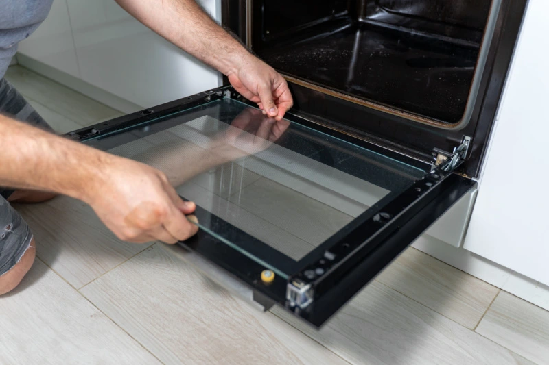Man removing glass from oven door.