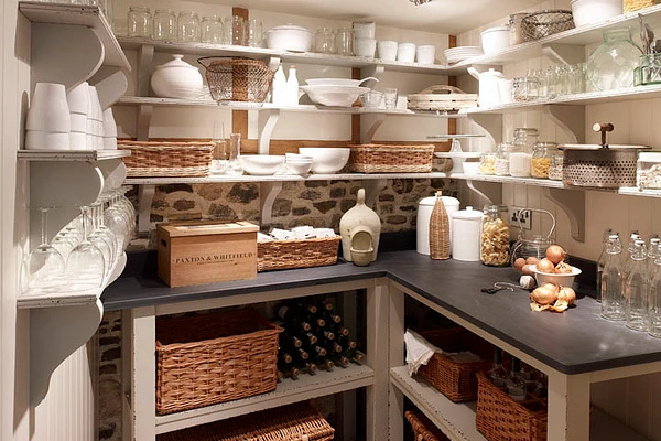 A well-organized kitchen pantry with open shelving showing jars, white ceramic containers, and baskets