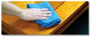 hand cleaning a wood table with a blue cloth