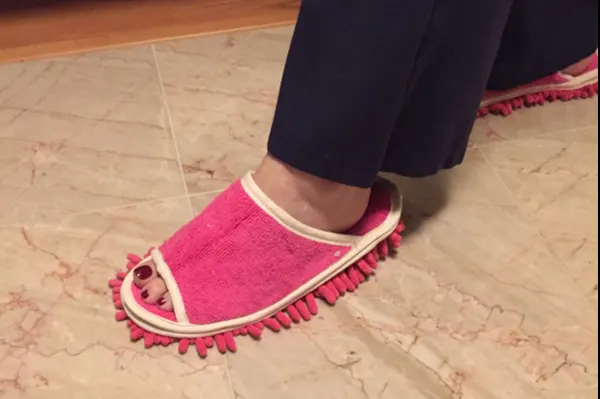 A woman's foot in a pink slipper with short mop tassels protruding from the bottom