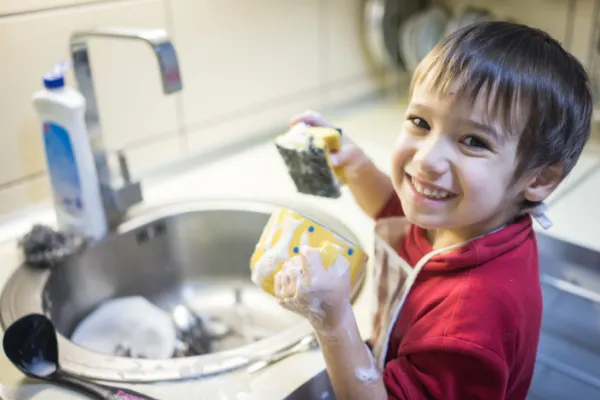  Little boy smiling while washing the dishes