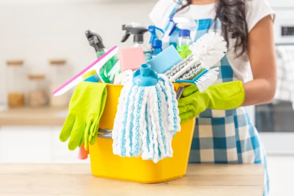 Woman holding bucket full of house cleaning supplies