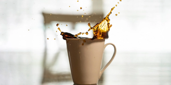 Coffee splashing out of tan mug.