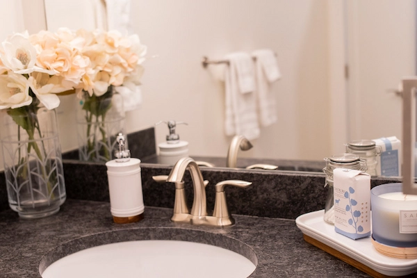 Black granite top bathroom sink with white hand soap dispenser and vase of flowers.