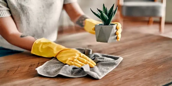 Person wearing yellow rubber gloves dusting furniture with cloth.