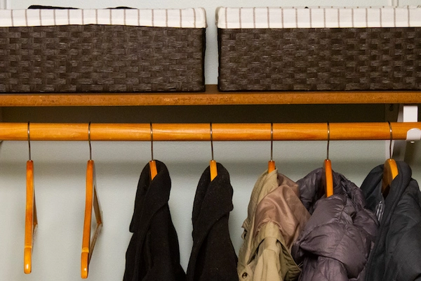 Close-up of two black wool coats and three puffer coats on wooden hangers in organized hall closet.