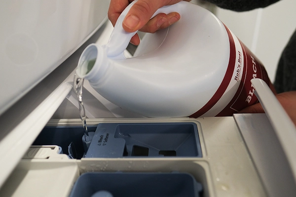 Person pouring chlorine bleach into automatic dispenser in washer.