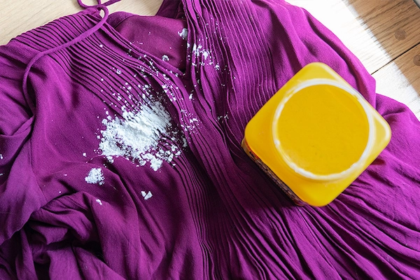 Overhead view of purple dress with large white stain and yellow container of stain remover.