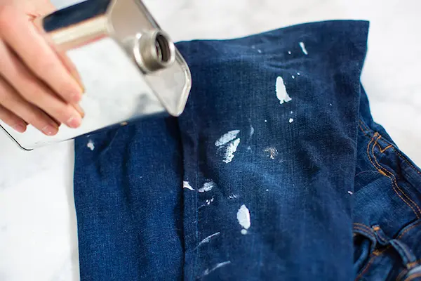 Close-up of person holding steel canister over blue jeans stained with white paint.
