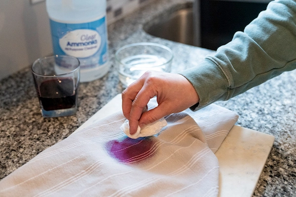 Close-up of person's hand blotting grape juice stain out of fabric with ammonia.