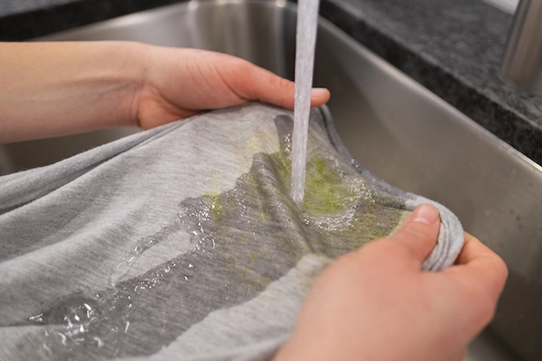 Person holding shirt with grass stains under running kitchen faucet.