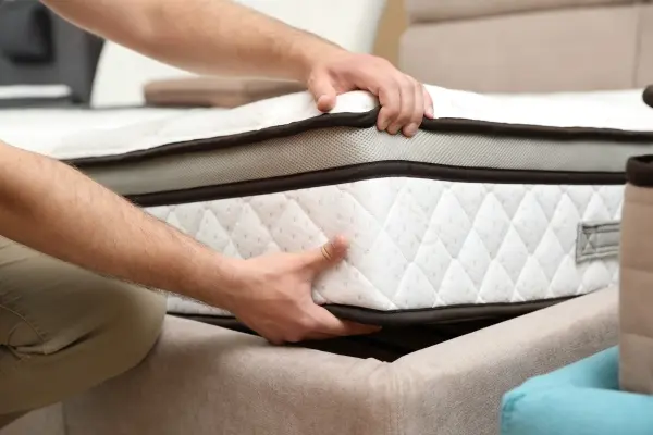 Closeup of person lifting a corner of the mattress off of a bed frame.