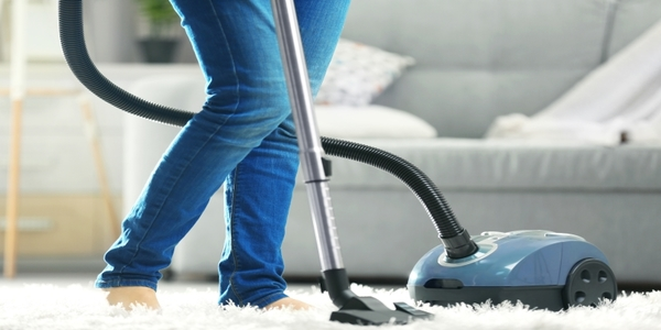 A person vacuuming a white rug in the living room.